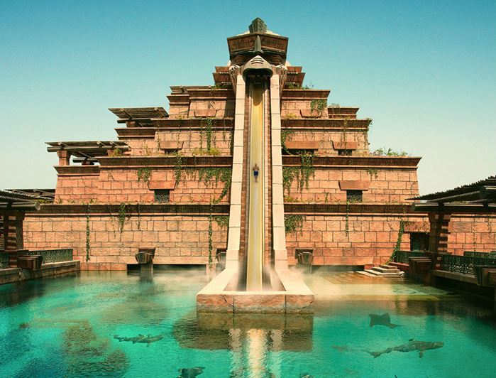 A water slide in a pool with Atlantis, The Palm in the background  Description automatically generated